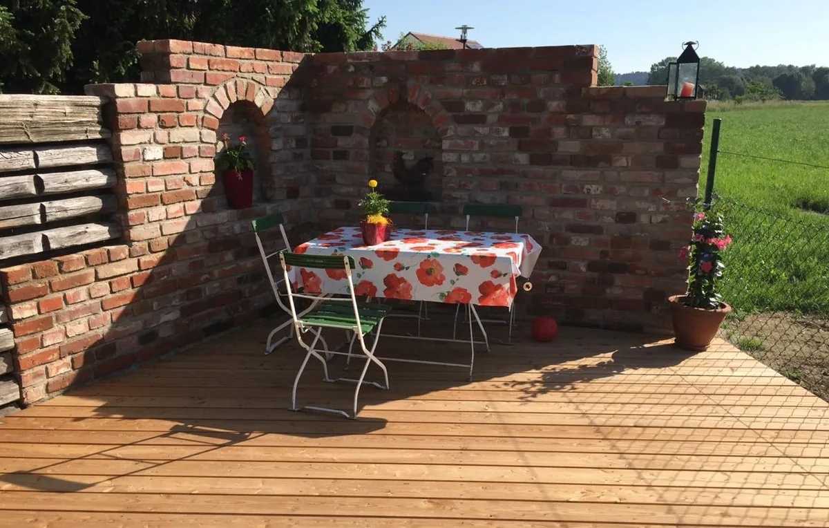 Backsteinmauer an Holzterrasse – gemauerte Mauer als Terrassenabschluss, natürlicher Charakter im Garten
