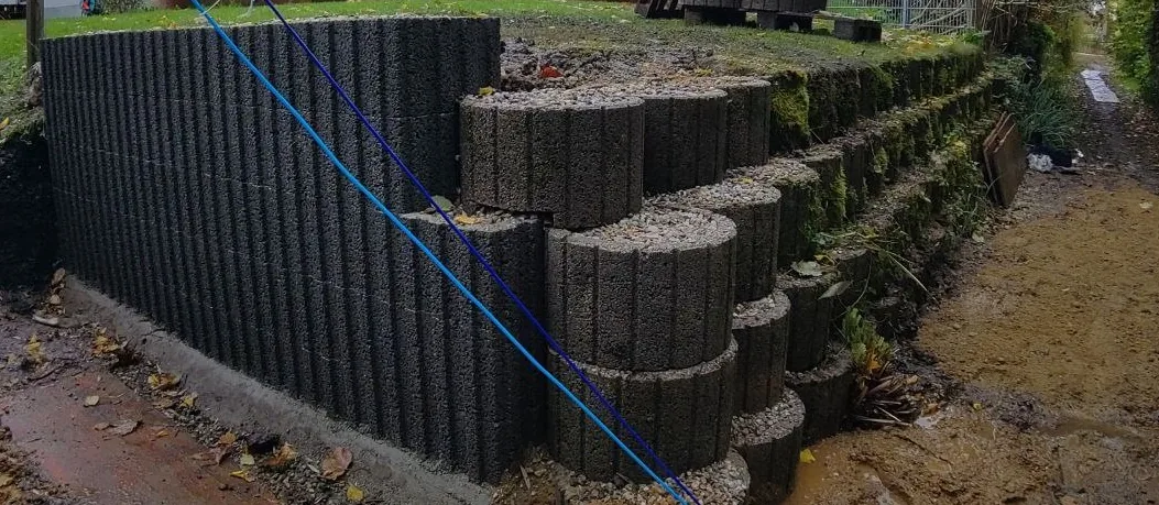 Stützmauer aus Betonringen im Aufbau – Ringe werden gestapelt und gesichert, Geländeabfangung sichtbar