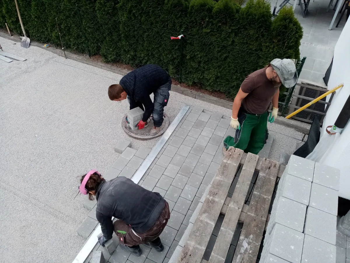 Handwerker verlegt Pflastersteine in Einfahrt – Rüttelplatte und Verlegehilfe im Einsatz