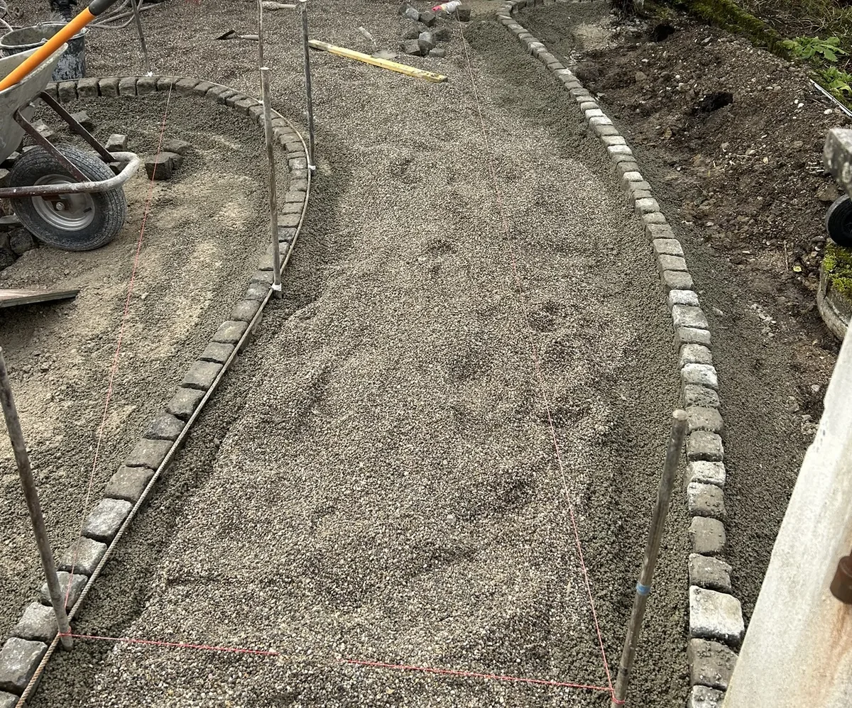 Randsteine werden an Gartenweg gesetzt – frisch eingebettete Betonbordsteine neben offener Pflasterfläche
