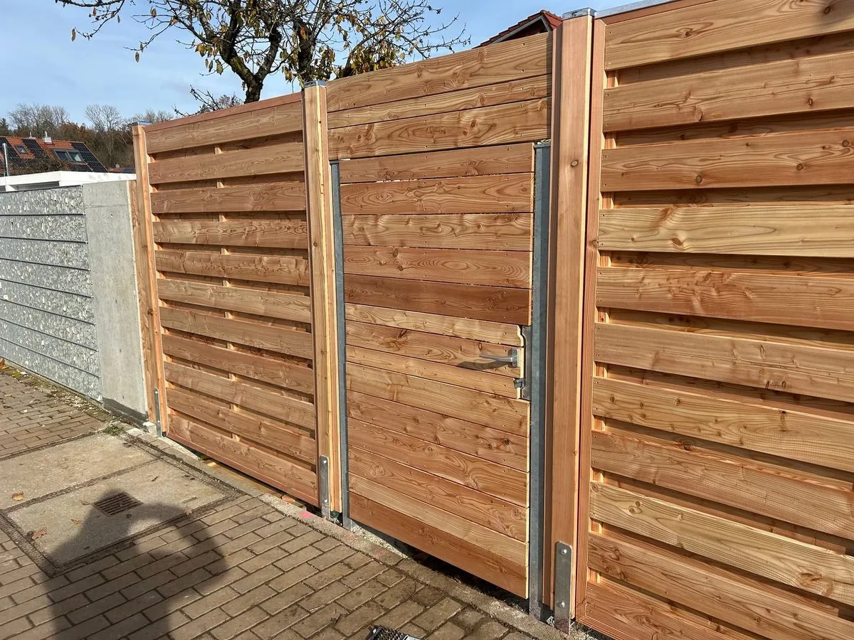 Holzsichtschutz mit integrierter Gartentür – dunkle Dielen, Metallanschläge, einheitliches Erscheinungsbild